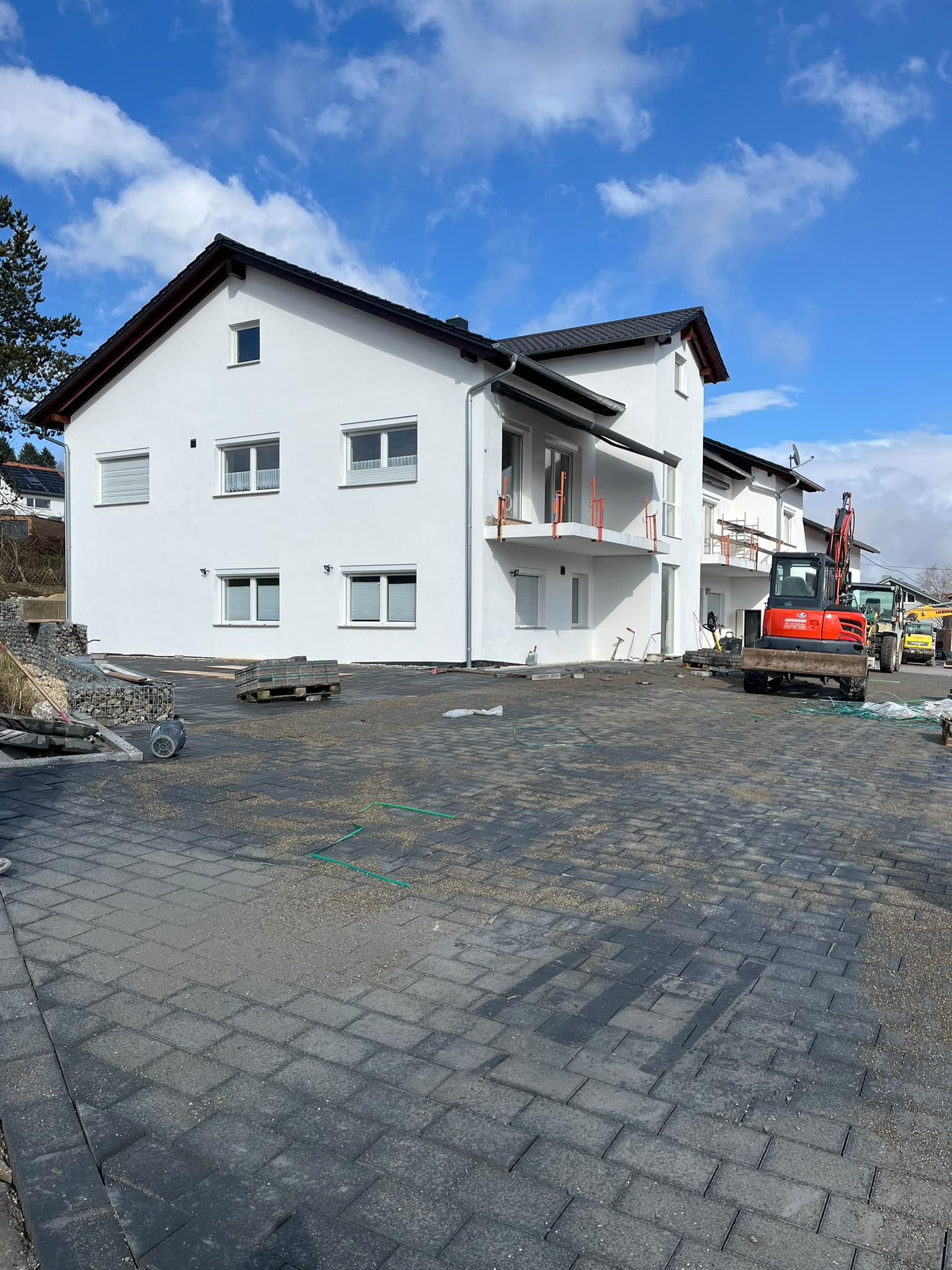 Neu gepflasterte Hoffläche vor einem Mehrfamilienhaus mit Bagger von Herrmann im Hintergrund